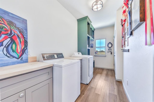 washroom featuring light wood finished floors, baseboards, cabinet space, and washing machine and clothes dryer