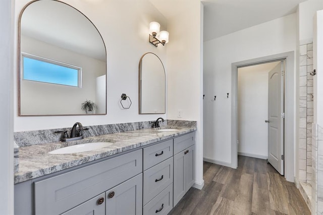 full bath with double vanity, baseboards, a sink, and wood finished floors