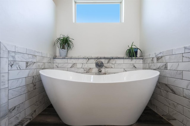 full bath with a wainscoted wall, a freestanding bath, and tile walls