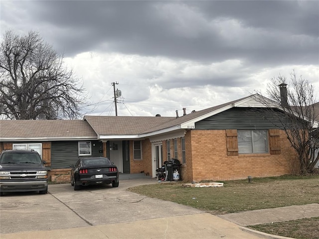 single story home featuring concrete driveway, brick siding, and a front lawn