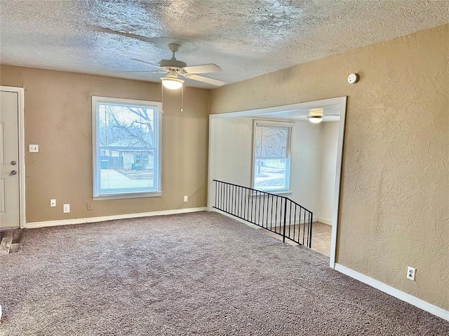 carpeted spare room with a textured ceiling, a textured wall, ceiling fan, and baseboards