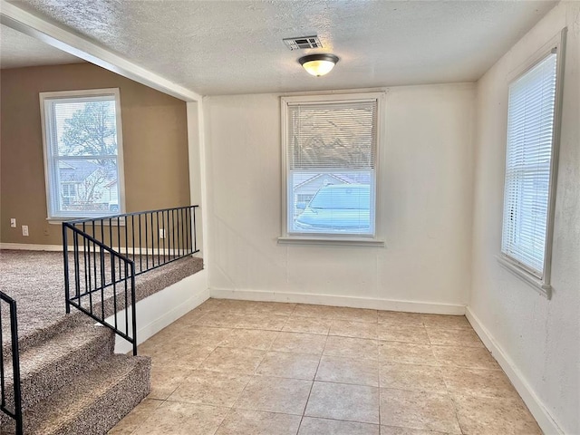 empty room with visible vents, a textured ceiling, baseboards, and light tile patterned flooring