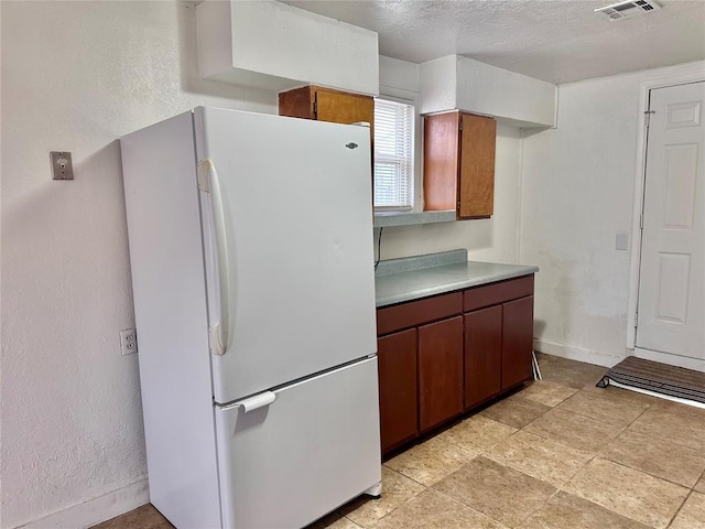 kitchen featuring a textured ceiling, a textured wall, visible vents, light countertops, and freestanding refrigerator