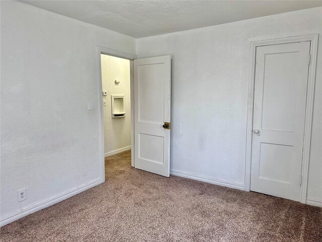 empty room with light carpet, baseboards, a textured ceiling, and a textured wall