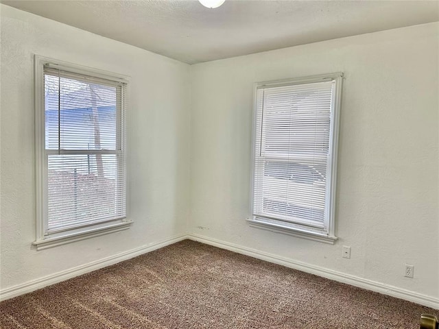 spare room featuring a textured wall, carpet floors, and baseboards