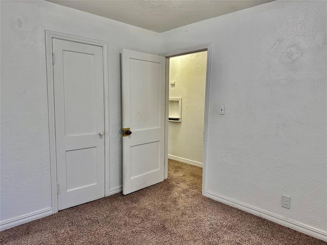 unfurnished bedroom with a textured ceiling, a textured wall, carpet, and baseboards