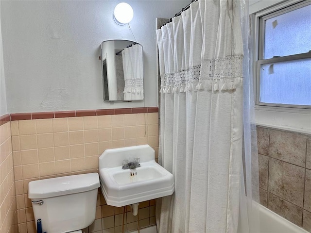 full bath featuring tile walls, toilet, shower / tub combo, wainscoting, and a sink