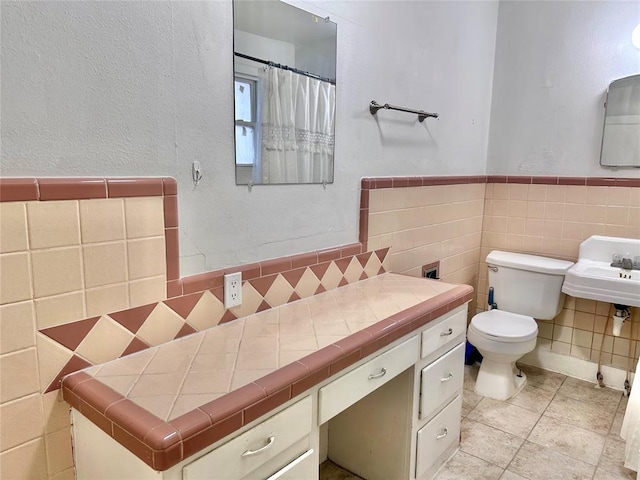 full bath with toilet, a sink, tile walls, wainscoting, and tile patterned floors