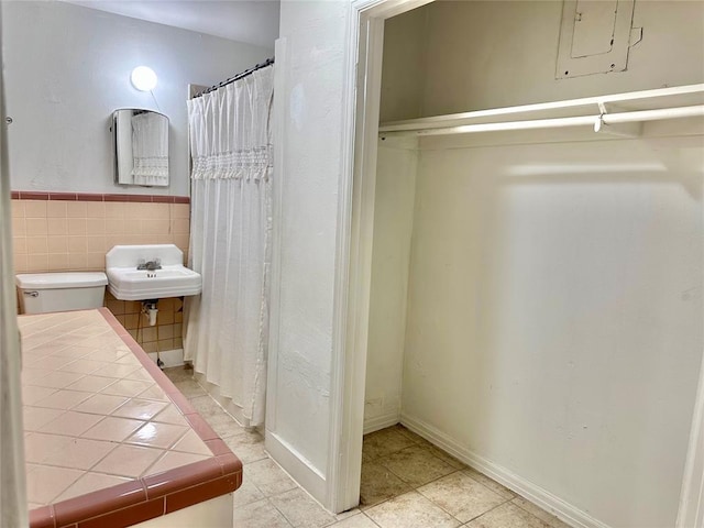 bathroom with wainscoting, toilet, tile patterned floors, a sink, and tile walls