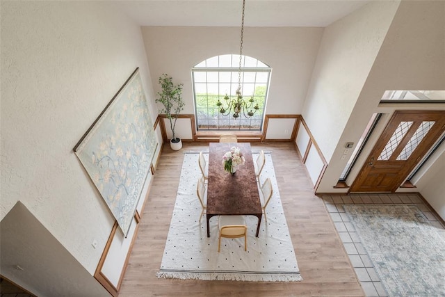 foyer entrance featuring light wood-style floors, an inviting chandelier, a textured wall, and vaulted ceiling