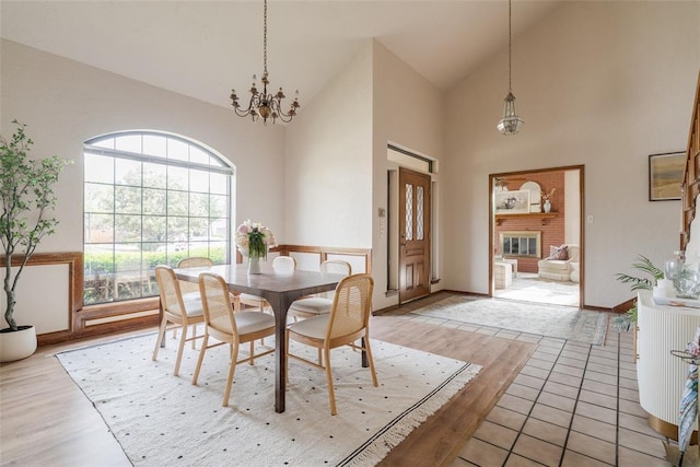 dining room with a chandelier, a fireplace, high vaulted ceiling, and light wood-style floors