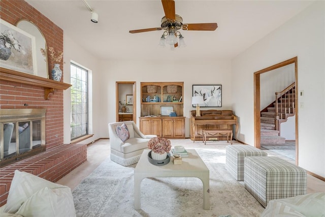 living area with track lighting, a ceiling fan, a brick fireplace, and stairway