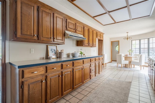 kitchen with hanging light fixtures, a notable chandelier, under cabinet range hood, brown cabinetry, and light tile patterned flooring