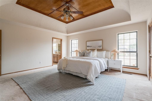 bedroom featuring a tray ceiling, baseboards, ensuite bath, and light carpet
