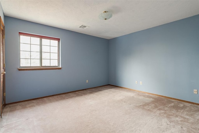carpeted empty room featuring visible vents, a textured ceiling, and baseboards