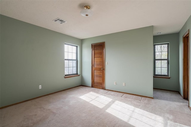 unfurnished bedroom featuring visible vents, multiple windows, and light carpet
