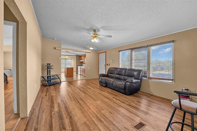 living room featuring a textured ceiling, a textured wall, visible vents, a ceiling fan, and light wood-type flooring