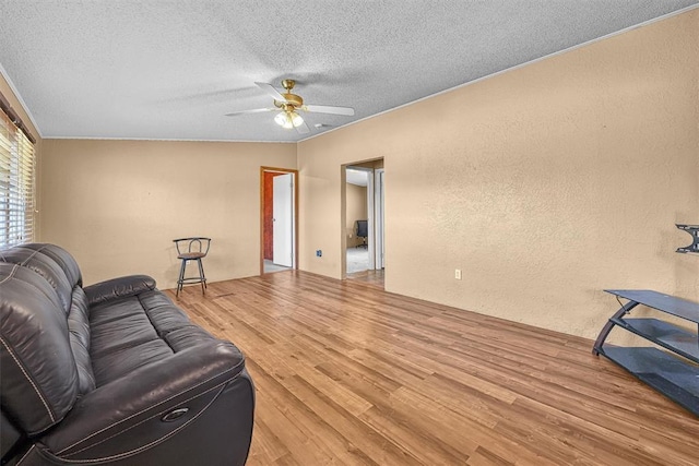 living room featuring a ceiling fan, a textured wall, a textured ceiling, and wood finished floors