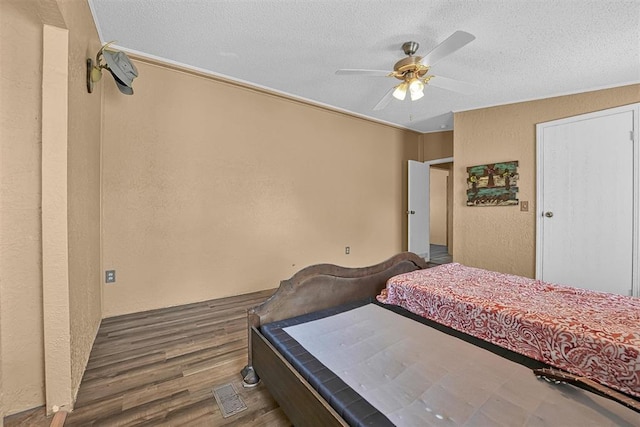 bedroom with visible vents, a textured wall, a ceiling fan, a textured ceiling, and wood finished floors