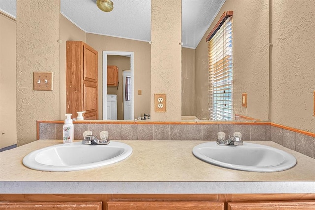 full bath with a textured wall, washer / clothes dryer, a sink, and double vanity