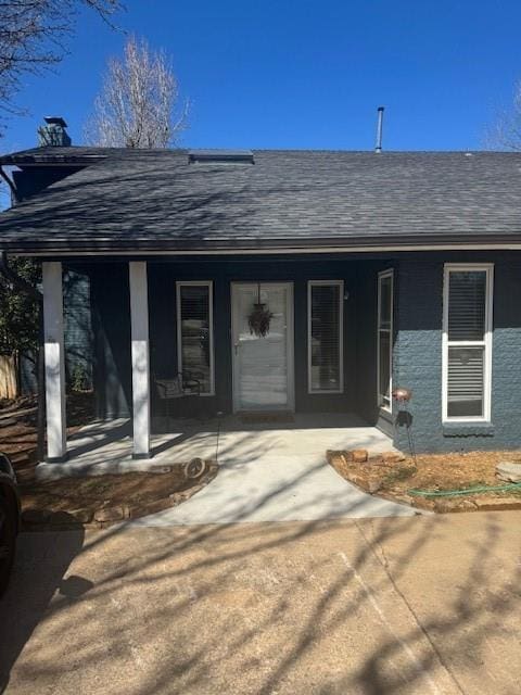 entrance to property featuring a porch and roof with shingles