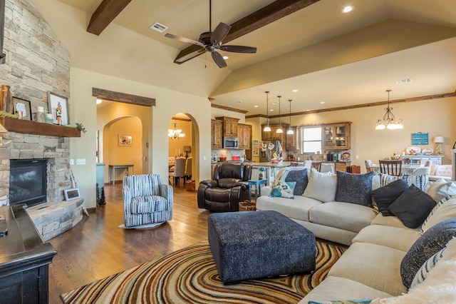 living room featuring arched walkways, lofted ceiling with beams, dark wood-style flooring, a fireplace, and visible vents