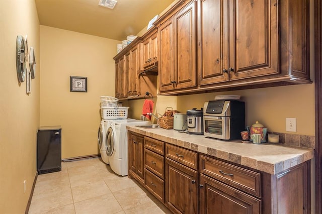 laundry room with light tile patterned flooring, washing machine and dryer, a sink, visible vents, and cabinet space