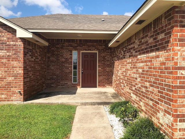 doorway to property featuring brick siding and a shingled roof