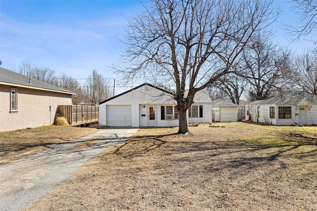 ranch-style house with a front lawn, fence, a garage, an outbuilding, and driveway