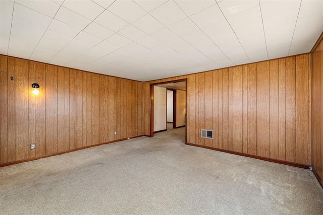 carpeted spare room featuring visible vents, baseboards, and wooden walls