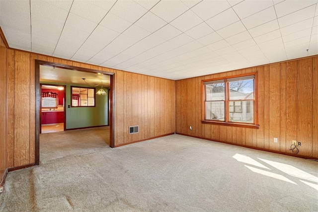 empty room with baseboards, wood walls, and carpet flooring