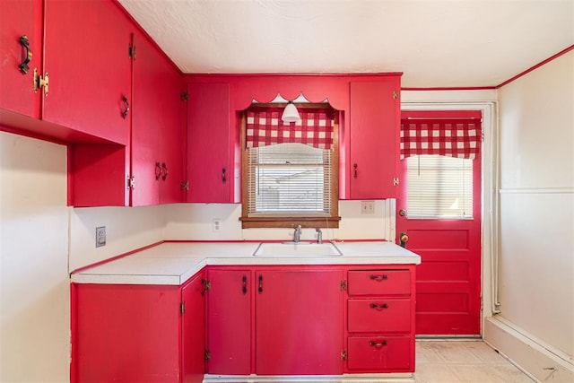 kitchen featuring a sink, light countertops, light tile patterned flooring, and red cabinets