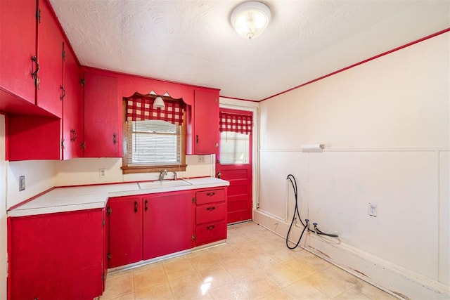 kitchen with a sink, a textured ceiling, red cabinets, light countertops, and light floors