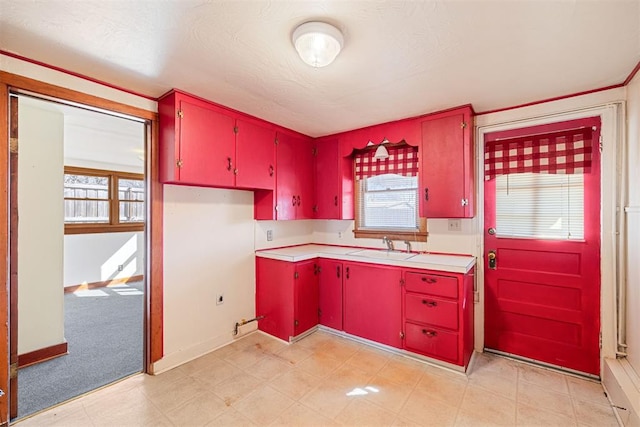 kitchen featuring a sink, red cabinets, a wealth of natural light, and light countertops