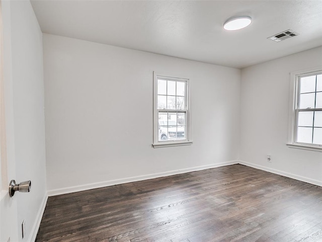 unfurnished room with visible vents, dark wood finished floors, and baseboards