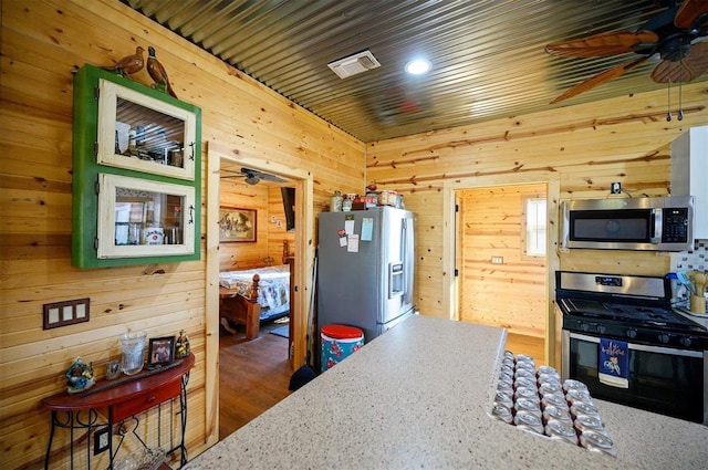 kitchen with wood walls, a ceiling fan, and appliances with stainless steel finishes