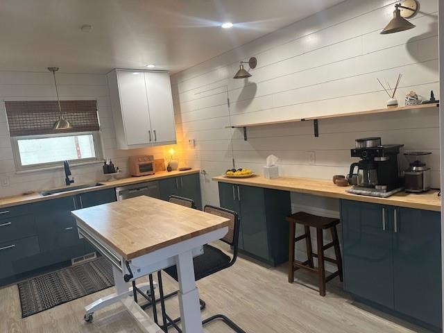 kitchen featuring a sink, hanging light fixtures, open shelves, light wood finished floors, and tasteful backsplash