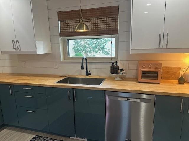 kitchen featuring white cabinets, a sink, hanging light fixtures, and stainless steel dishwasher