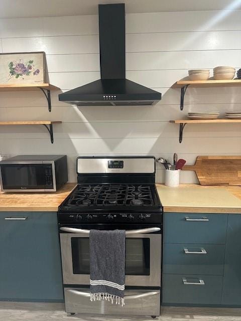 kitchen with stainless steel gas stove, blue cabinets, wall chimney range hood, open shelves, and backsplash