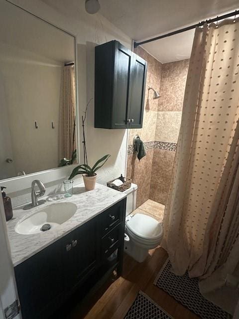 bathroom featuring wood finished floors, tiled shower, vanity, and toilet