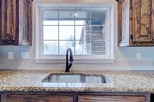 kitchen featuring light stone countertops, a textured wall, and a sink