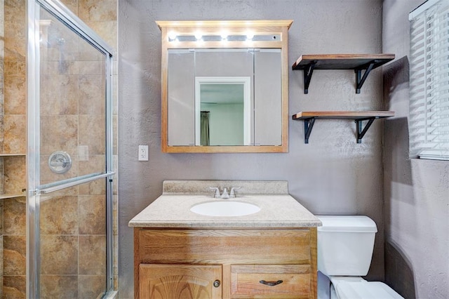 bathroom featuring vanity, toilet, a textured wall, and a stall shower