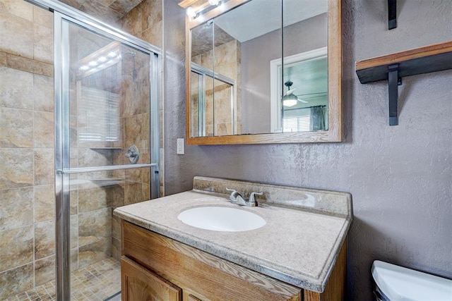 full bathroom featuring a shower stall, toilet, a textured wall, vanity, and a ceiling fan