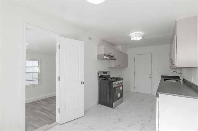 kitchen featuring stainless steel gas stove, dark countertops, marble finish floor, under cabinet range hood, and a sink