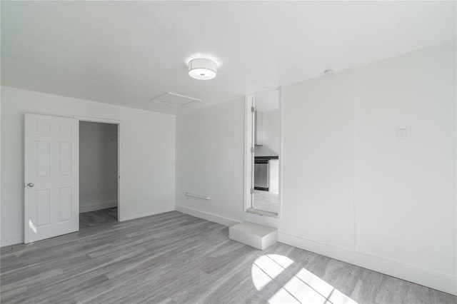 unfurnished room featuring attic access, baseboards, and wood finished floors