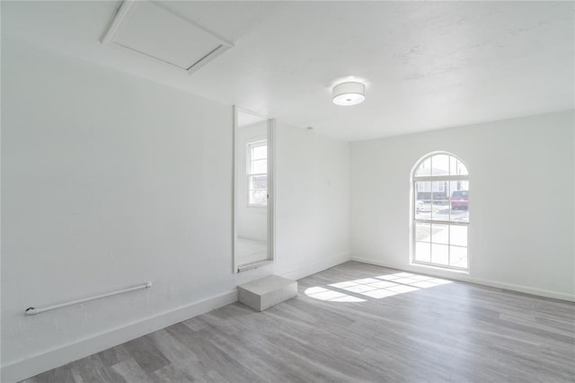 spare room featuring attic access, a healthy amount of sunlight, baseboards, and wood finished floors