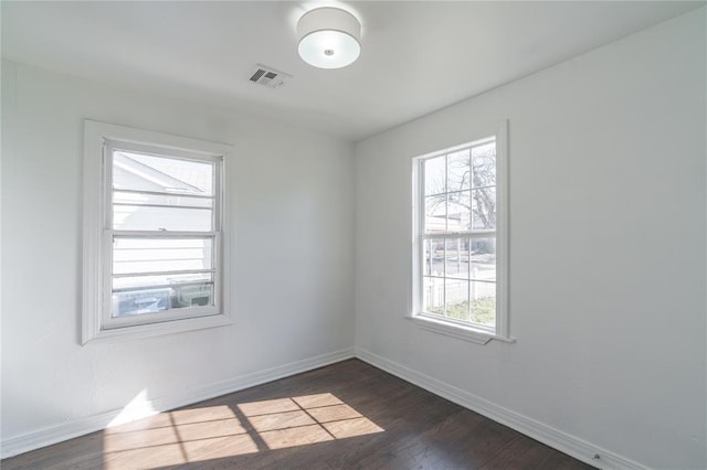 unfurnished room with dark wood-style floors, visible vents, and baseboards