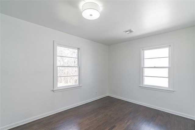 empty room featuring dark wood-style flooring, plenty of natural light, visible vents, and baseboards