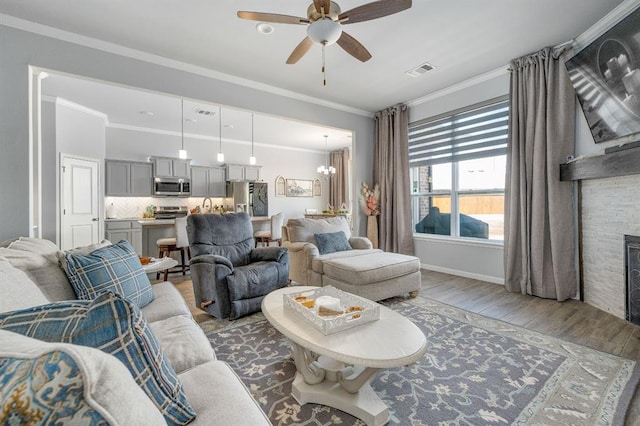 living room with visible vents, wood finished floors, a stone fireplace, and ornamental molding