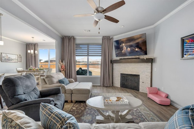 living area with wood finished floors, baseboards, a fireplace, ornamental molding, and ceiling fan with notable chandelier